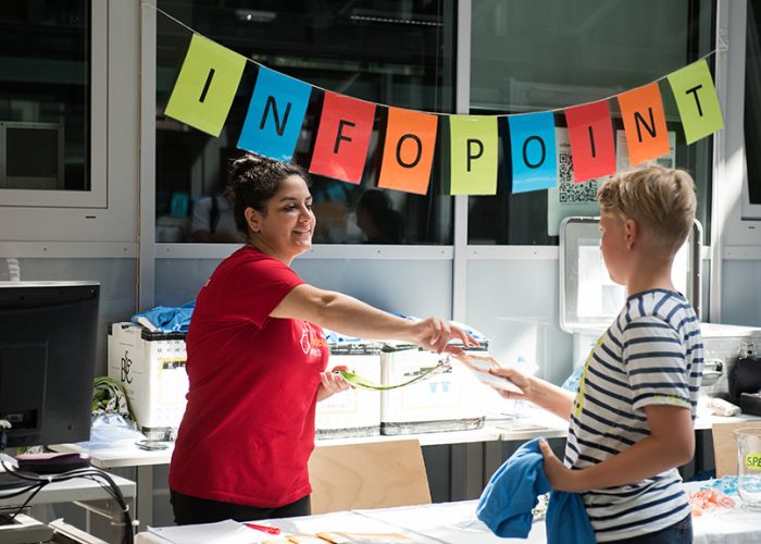 ein KinderuniWien-Student zeigt seinen Ausweis am InfoPoint her