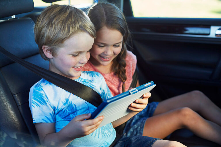 a girl and a boy sit in the car and look at something on the tablet