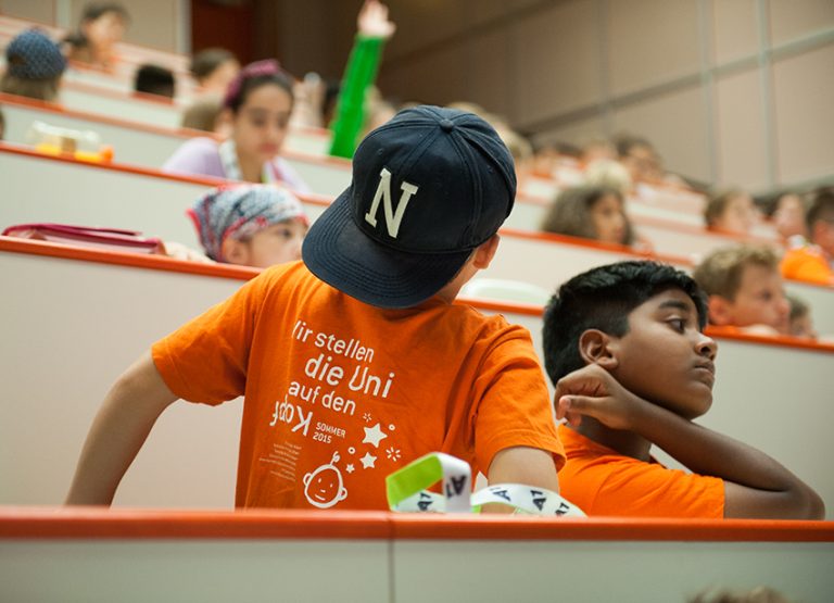 Children in the lecture hall. On the back of the T-shirt it says: We turn university upside down.