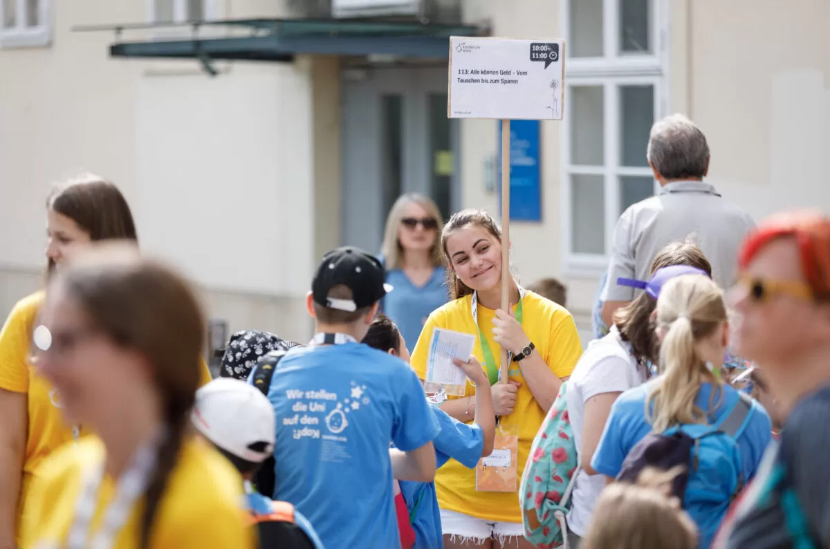 beim Treffpunkt wird ein Lehrveranstaltungsschild von einem Teammitglied hochgehalten