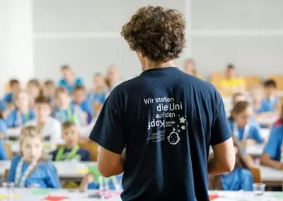 ein Lehrender trägt das KinderuniWien T-Shirt mit dem Motto "Wir stellen die Uni auf den Kopf!"