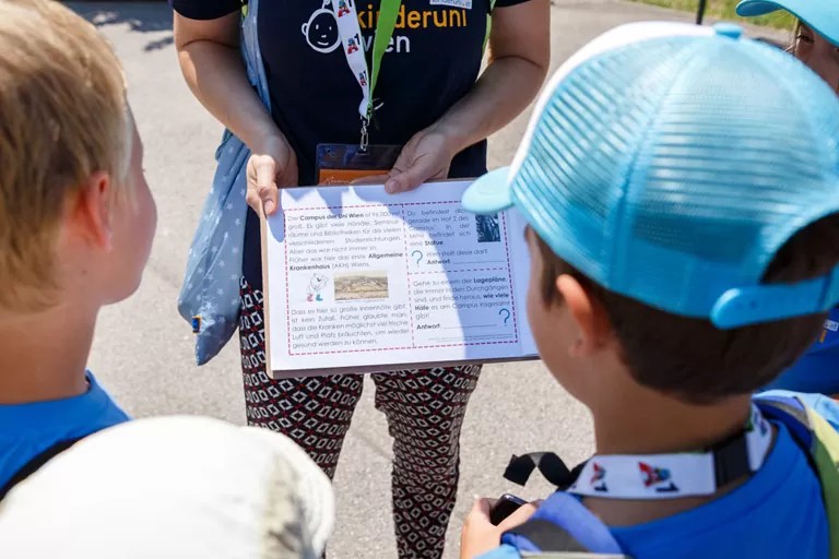 eine KinderuniWien Lehrende zeigt Kindern ein Arbeitsblatt